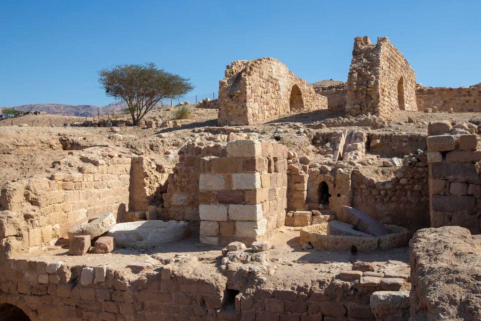 Photograph of the stone ruins of a sugar mill at Zoara in Jordan. The photo shows two partial walls in the background and other stone ruins in the foreground.